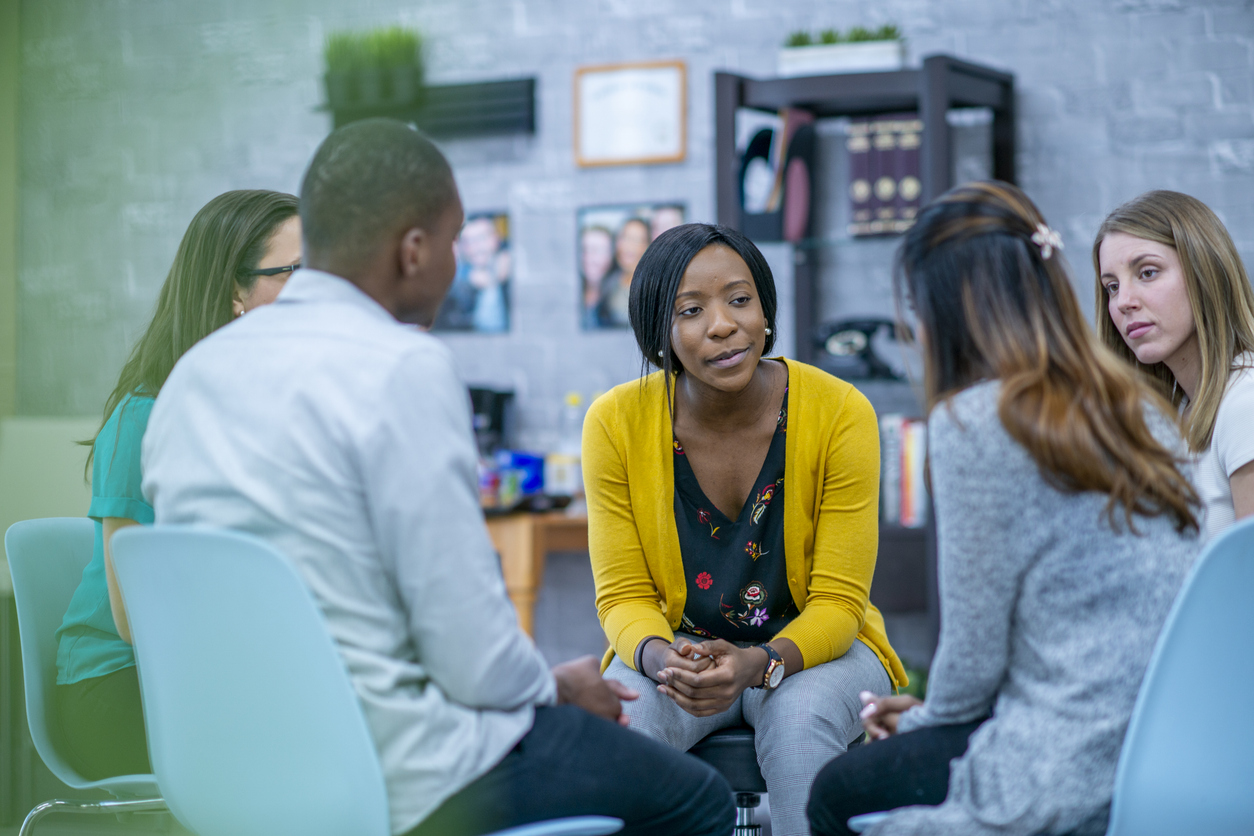 An attentive group of people sit in a circle listening to one of them speak.