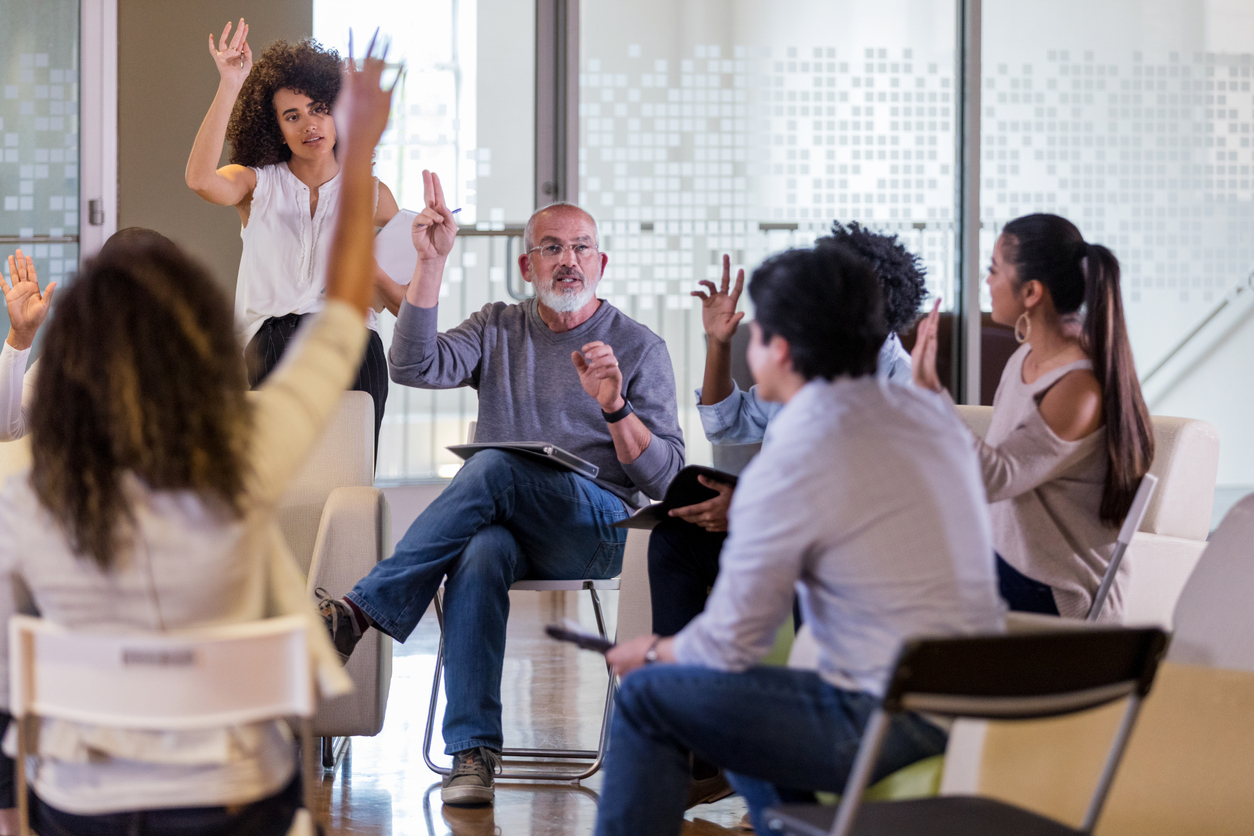 Men and women sit in a circle and raise their hands.