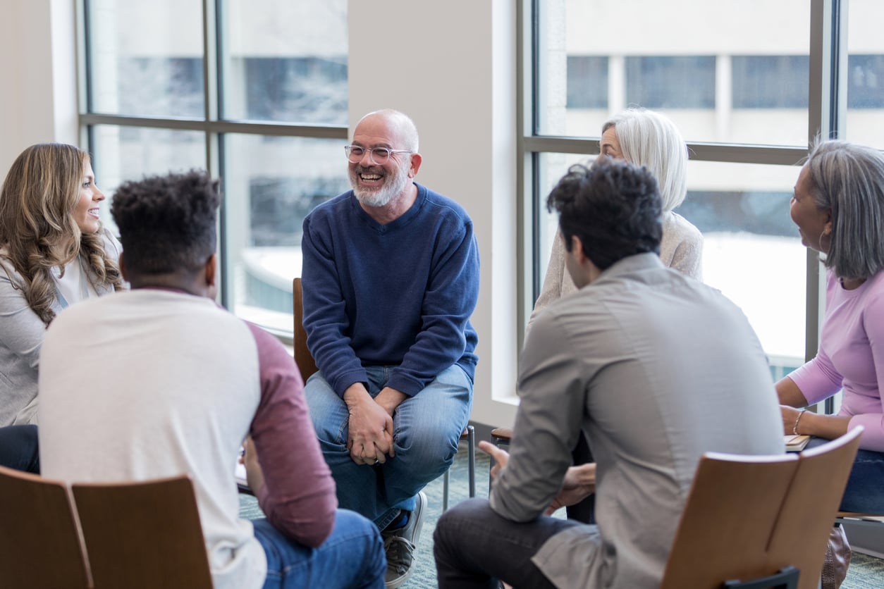 A group of men and women sit in a circle smiling.
