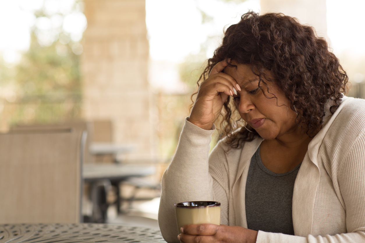 An unhappy looking woman sits at a table holding her head.