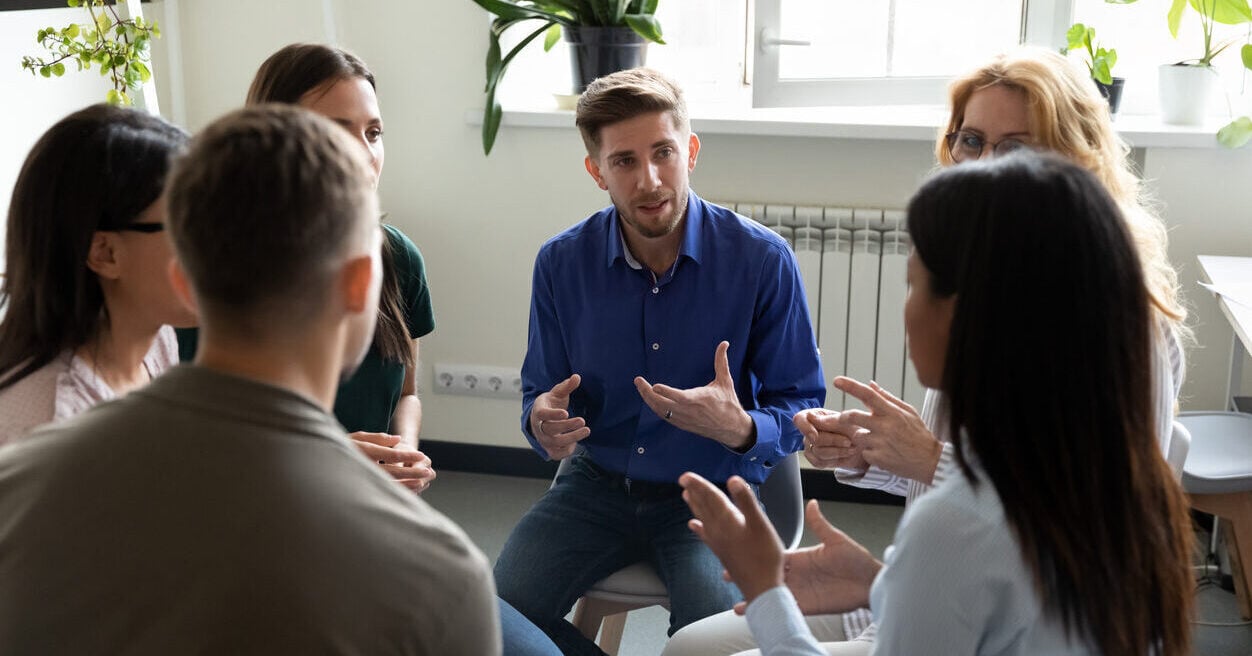 A group of six people sit talking in a circle.