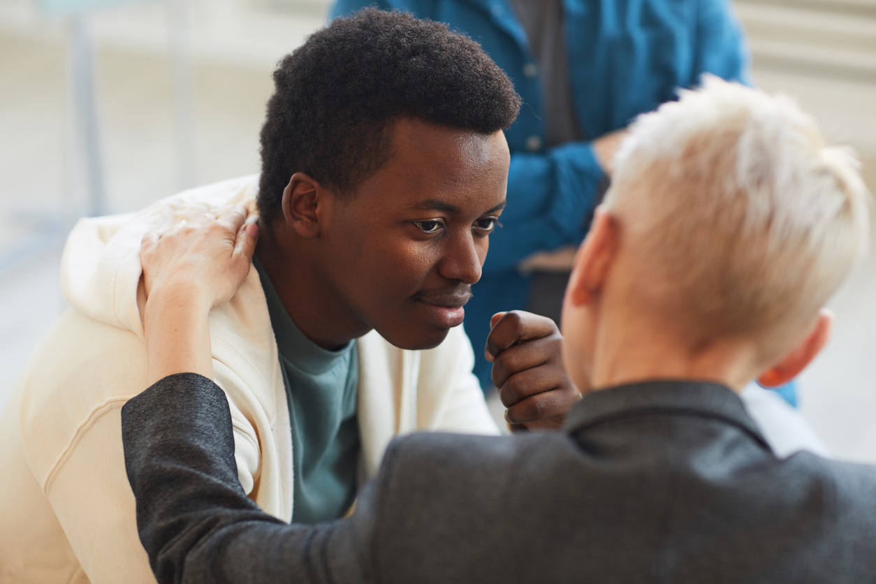 Someone reassures a man by touching him on shoulder in a group circle.