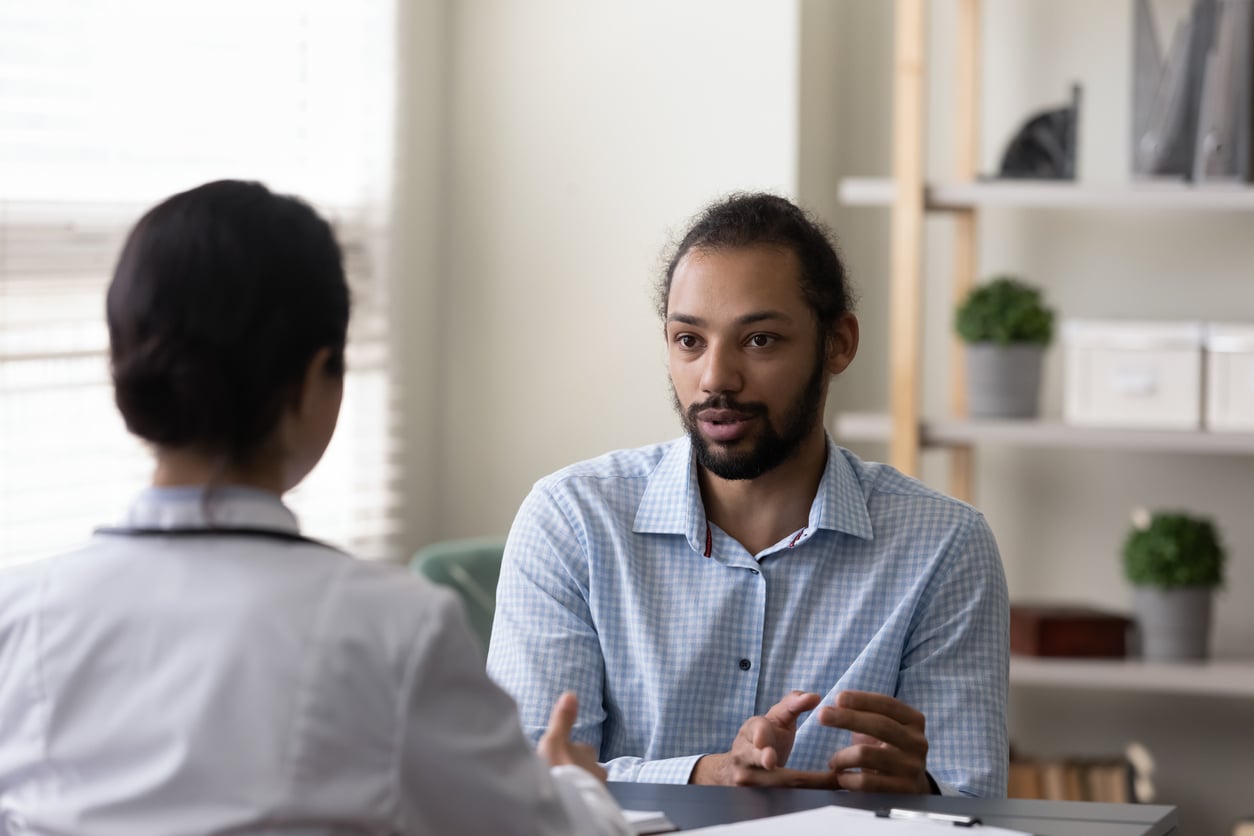 A concerned young man talks with the woman sat opposite him in an office.