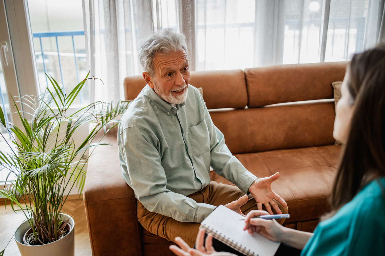 A man sits on a sofa talking to a therapist who takes notes.