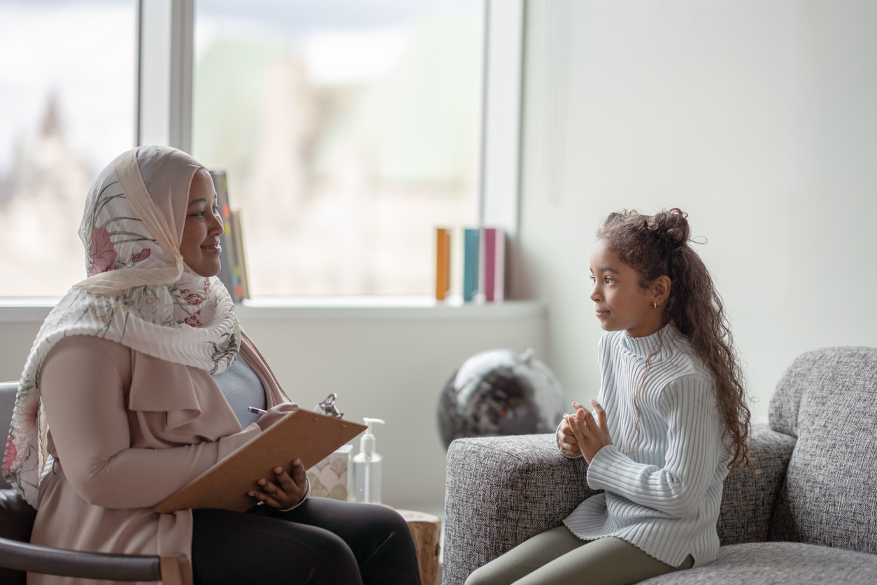 A smiling therapist sits opposite a young girl and makes notes.