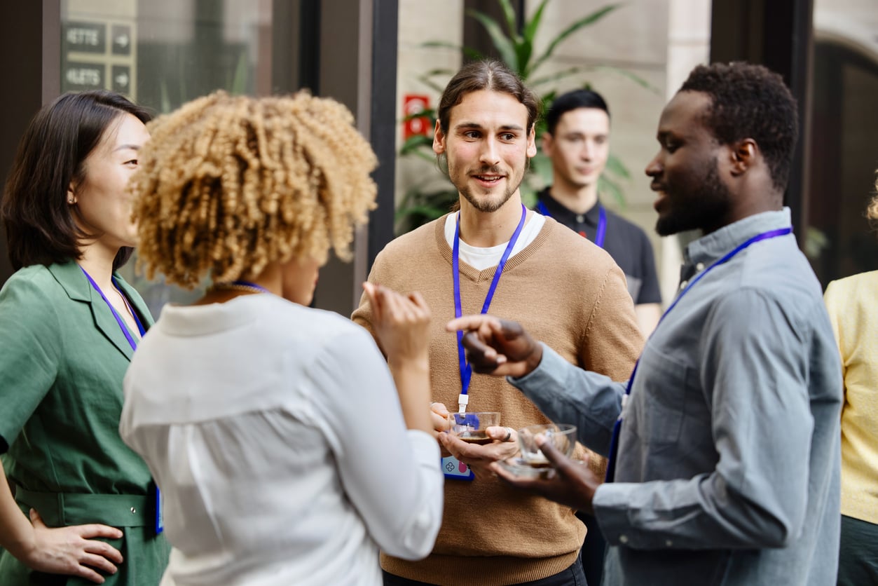 Two men and two women wearing lanyards smile, talk and drink coffee at an event.