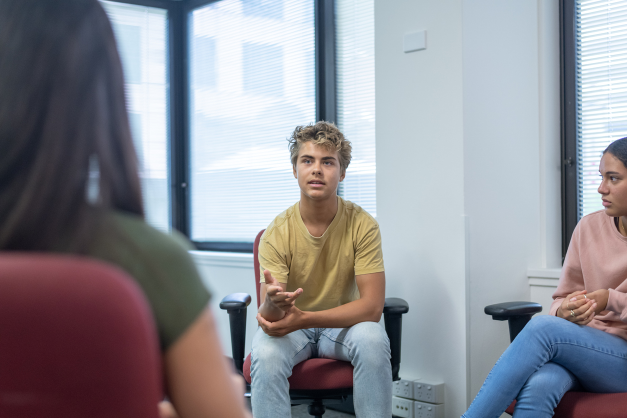 A young man speaks in a small group of young people sitting in a circle.