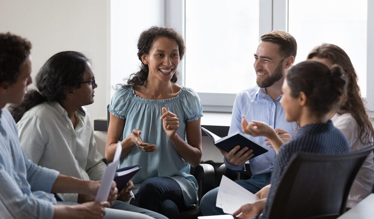 A group of men and women sit in a circle talking.