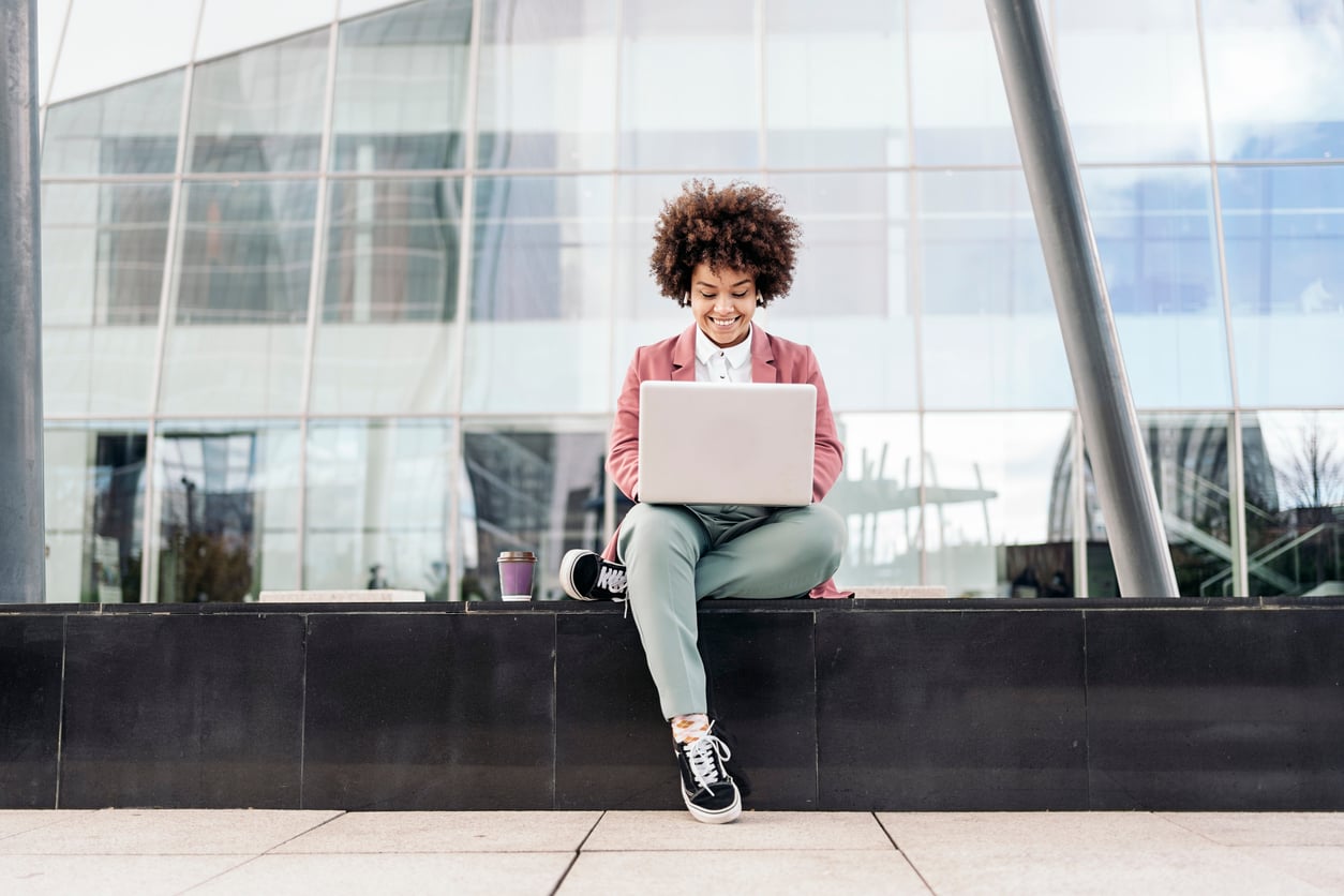 A woman sitting using a laptop outside of an office building.
