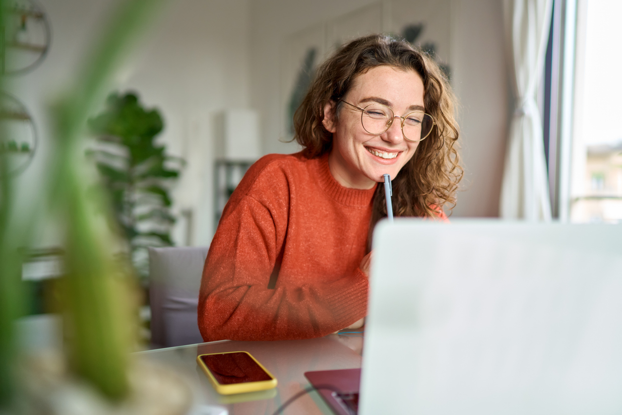 A smiling woman holding pen in front of a laptop.