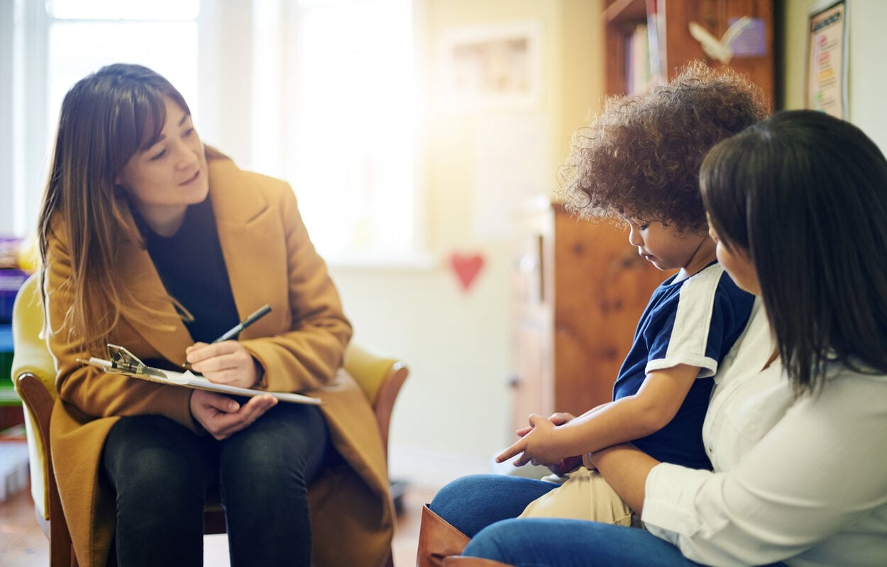 A therapist takes notes while talking to a mother and her worried-looking young child
