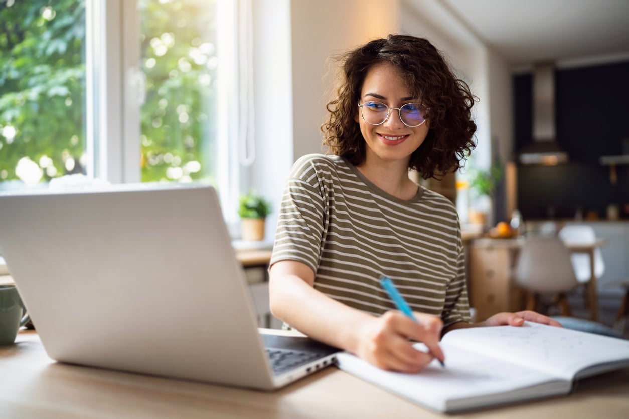 A young woman studying at home with laptop and notebook.