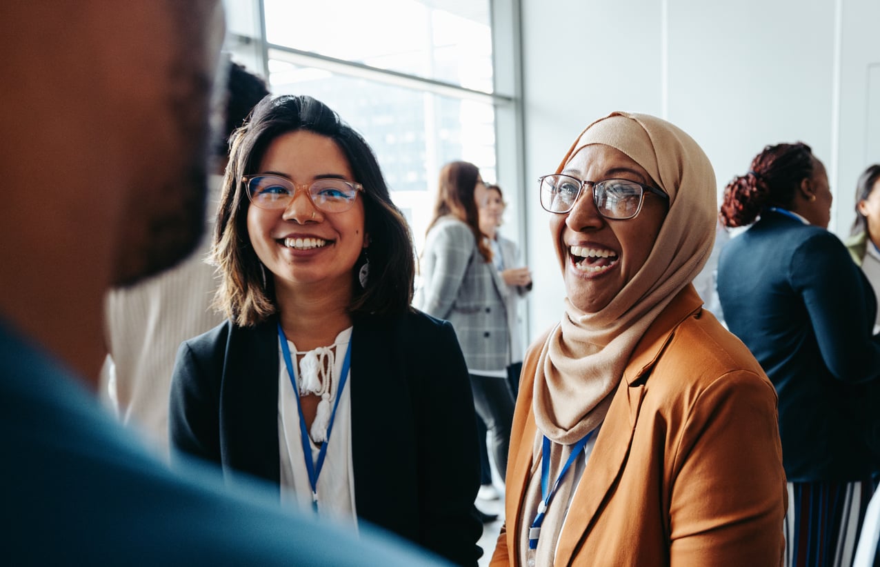 Two women laugh as they talk to a man at a group event.