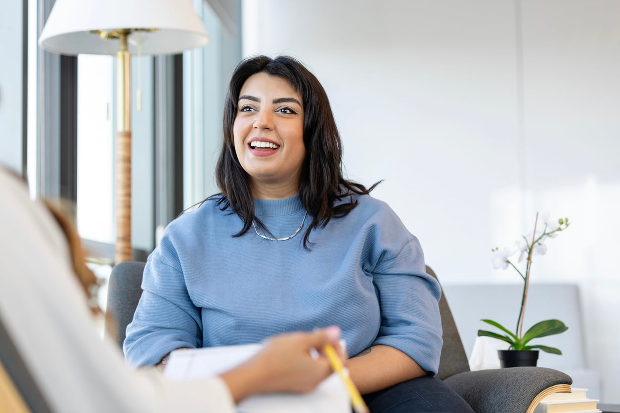 A woman smiles as she listens to her therapist, who is making notes.