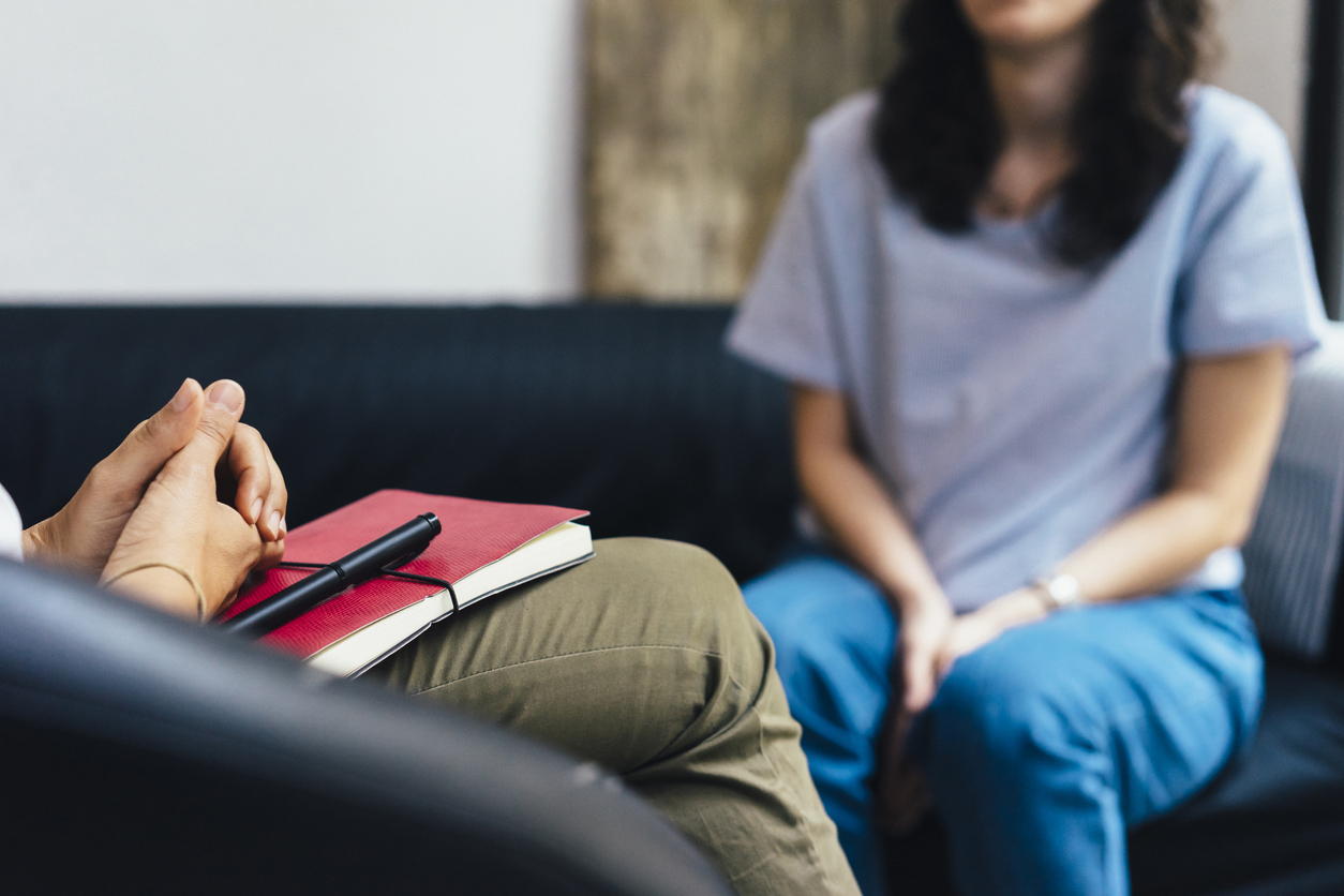 A woman sits talking to a therapist with a notebook.